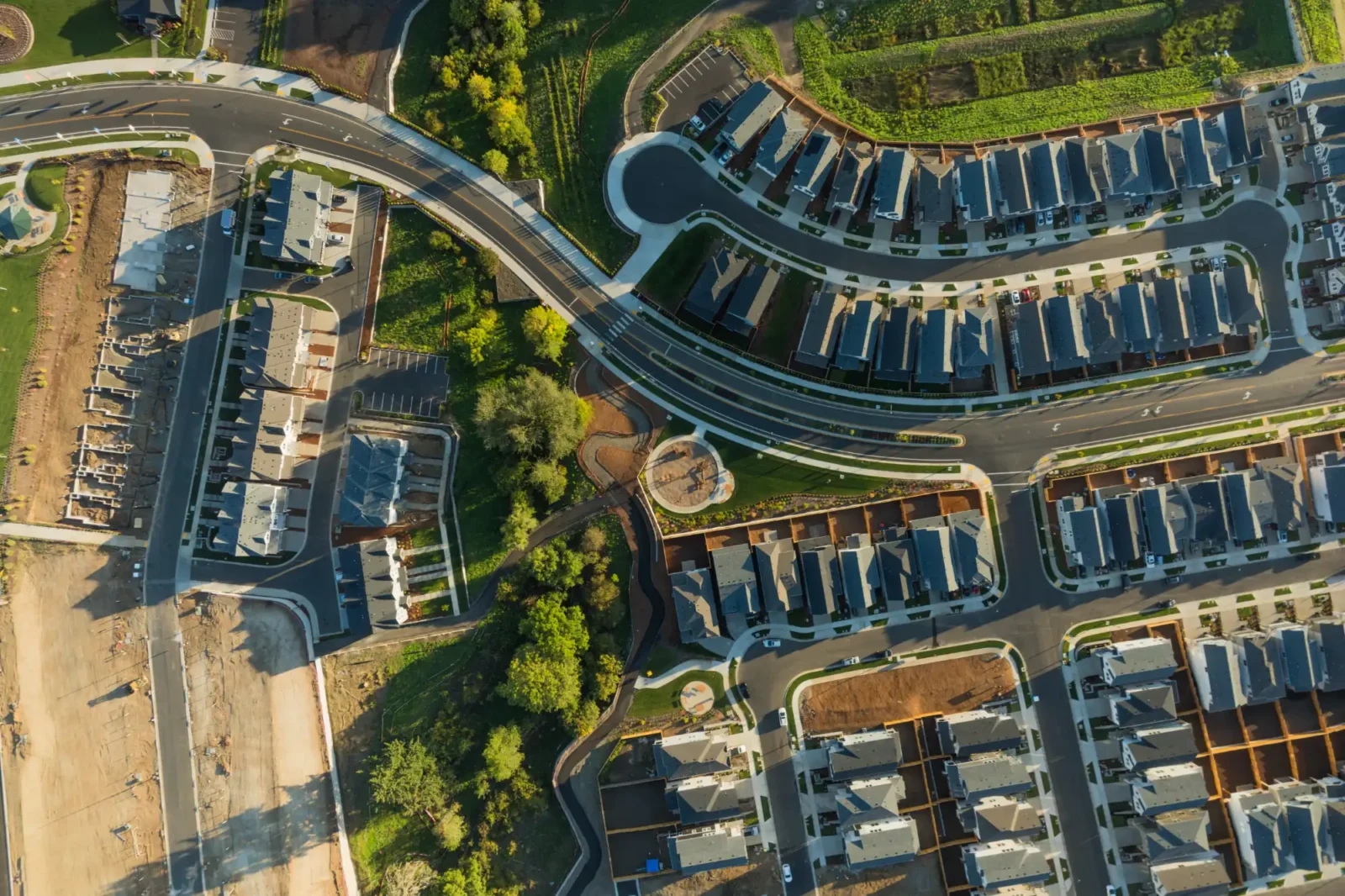 An aerial photo of a new suburban residential neighborhood with uniform housing units, paved streets, and adjacent land cleared for ongoing construction.